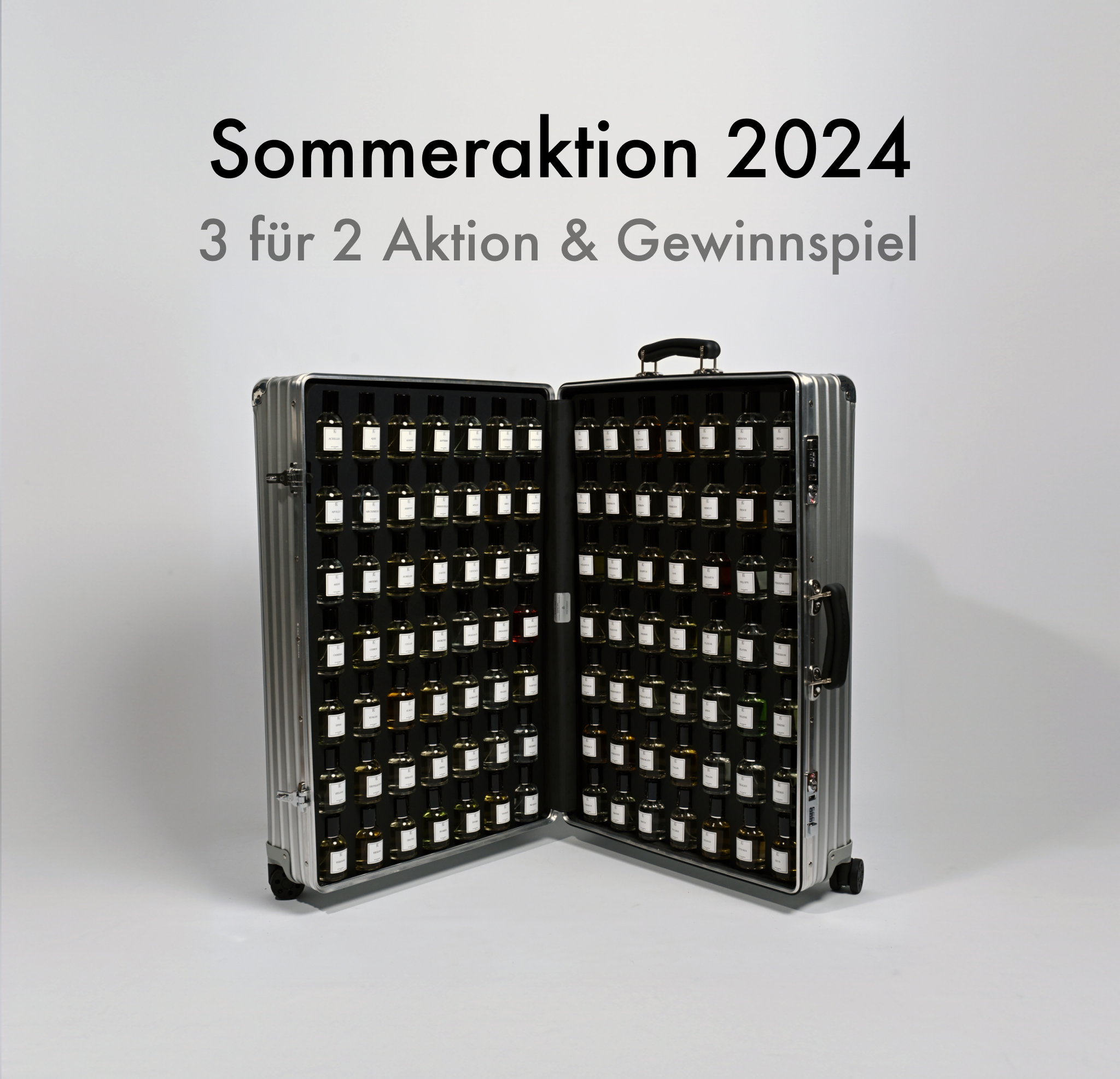 Ein silberner Koffer mit schwarzem Innenfutter steht geöffnet auf hellem Boden, darin viele kleine Fläschchen in mehreren Reihen. Darüber steht in schwarzer Schrift: „Sommeraktion 2024 3 für 2 Aktion & Gewinnspiel“. Der Koffer hat Rollen und Griff, jedes Fläschchen trägt ein weißes Etikett.