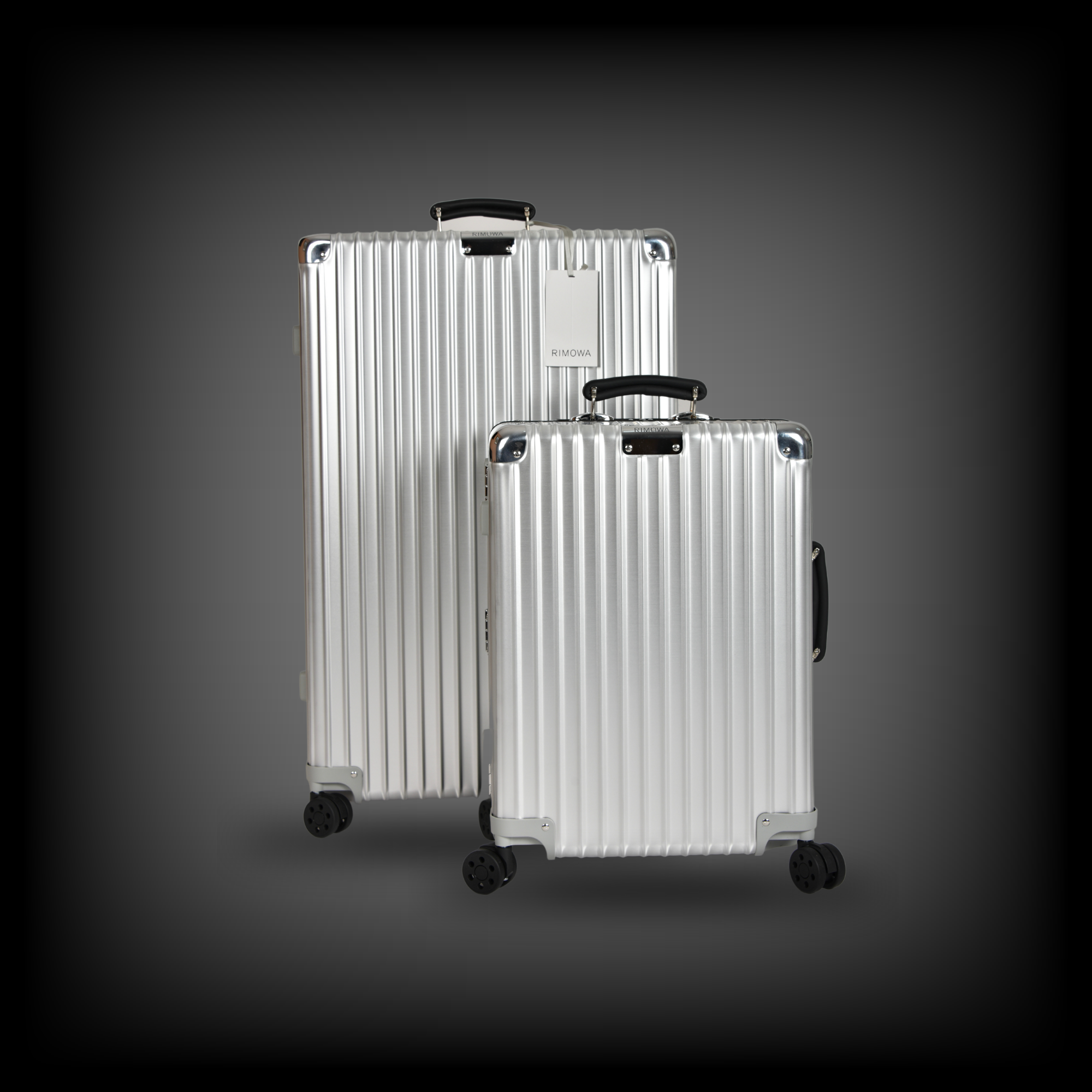 Zwei silberfarbene Koffer mit Rillenmuster, robusten schwarzen Griffen und vier Rollen, einer größer, einer etwas kleiner.