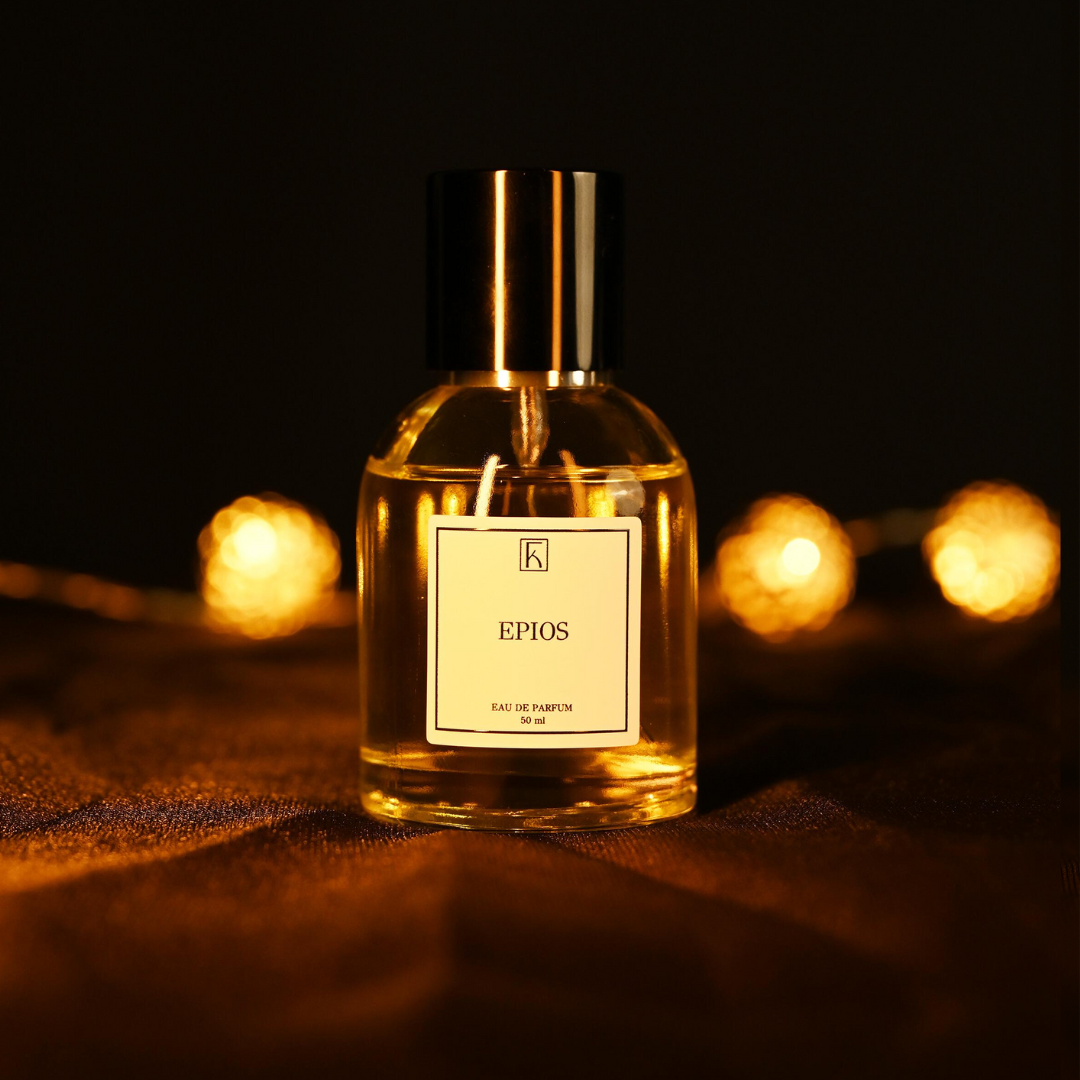 Eine runde Glasflasche mit goldener Flüssigkeit und schwarzem Verschluss steht auf dunklem Stoff. Das Etikett zeigt „EPIOS“. Im Hintergrund sind unscharfe, warme Lichterketten zu sehen.